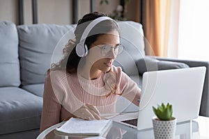 Focused millennial woman in headphones study on laptop at home