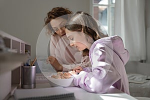 Focused mom helping teenage daughter doing homework studying from home