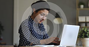 Focused motivated young indian female student studying on online courses.