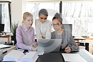 Focused multiracial female employees work on laptop together