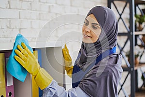 Focused Muslim woman wiping the bookshelves with a rug