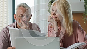 Focused pensive elderly retired married couple holding paper documents checking analyzing calculating bills bank loan