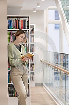 Focused pensive mature woman bookworm reading book in library. Lifelong learning