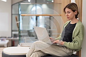 Focused pensive middle-aged woman freelancer working on laptop in library