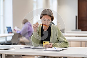 Focused pensive middle-aged woman using mobile app while studying online in library