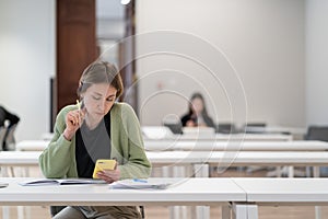 Focused pensive middle-aged woman using mobile app while studying online in library
