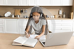 Focused pre teen schoolkid girl in headphones studying from home photo