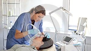 Focused professional female cosmetologist performing hardware procedure on aged woman patient, using airbrush to apply