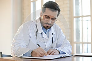 Focused 35s male doctor gp physician working with registry book. photo