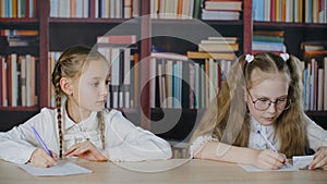 Focused schoolgirls writing exam and cheating in classroom