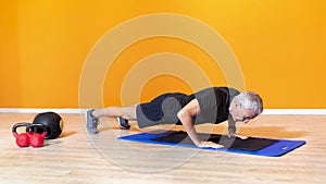 Focused senior fit man doing push up workout exercise laying at the gym  on orange background. mature people fitness