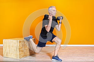 Focused senior fit man doing weight lifting workout exercise staning at the gym  on orange background. mature people