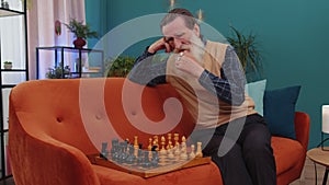 Focused senior grandfather man playing chess leisure board game alone, domestic activity at home