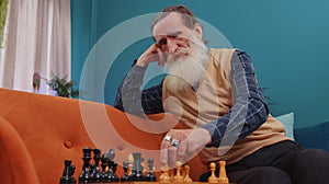Focused senior grandfather man playing chess leisure board game alone, domestic activity at home
