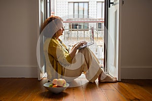 Focused senior woman sitting on floor by the balcony and using laptop