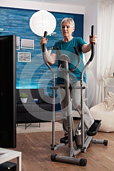 Focused senior woman working muscle legs doing body exercise using cycling bicycle machine