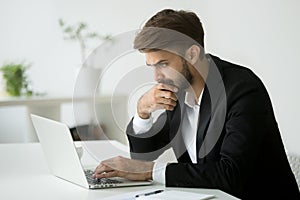 Focused serious businessman thinking reading online news using l