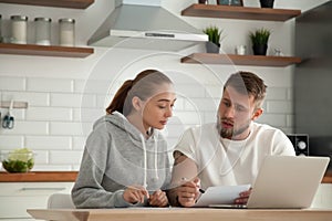 Focused serious couple checking bills sitting together at kitche