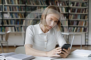 Focused serious female student using online app on mobile phone