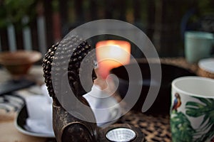 Focused shot of Buddha statue head on the table with a traditional Asian tea set in the background