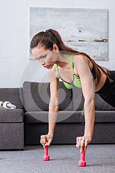 Focused sportswoman doing push ups with dumbbells