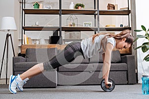 Focused sportswoman exercising with ab wheel