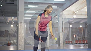 Focused sportswoman serving tennis ball in gym. Portrait of concentrated confident Caucasian woman training on indoor