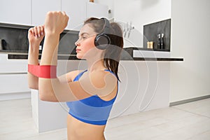 Focused sportswoman workout at home, using elastic resistance band on arms, stretching exercises in living room