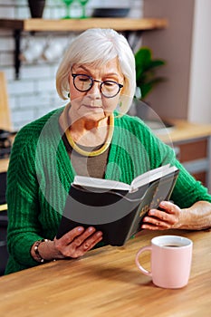 Focused stylish septuagenarian woman attentively considering the Bible lines