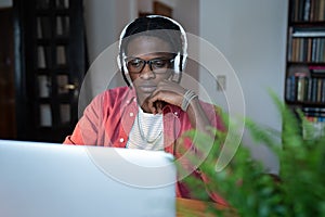 Focused successful African American man IT developer in headphones is works sits at desk with laptop