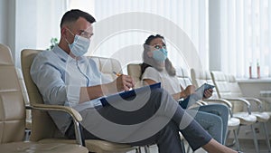 Focused successful business people in coronavirus face mask sitting on seminar indoors asking questions. Side view