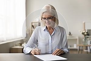 Focused successful mature old business woman in glasses signing contract