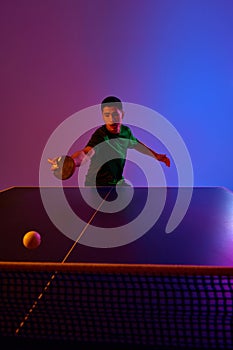 Focused table tennis player in green sportswear, keeping eye on ball, preparing for forehand shot against gradient