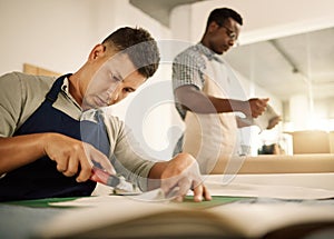 Focused tailor using knife to cut a piece of fabric. Mixed race designer trimming a piece of material. Young businessman