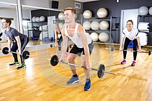 Focused team doing deadlift exercises with weights at fitness gym