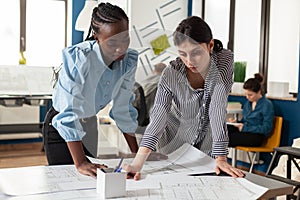 Focused team of women architects inspecting construction plans standing at desk