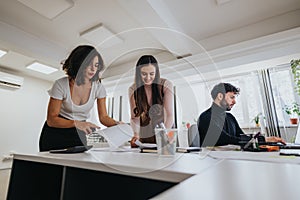 Focused team at work in a modern office: Two women collaborating and a man typing on a computer