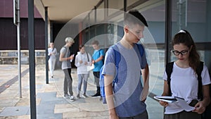 Focused teen boy talking to girl classmate outdoors in college campus, discussing schoolwork