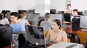 Focused teenager students sitting at desk in computer room with pc, preparing for exam. Focus on young girl