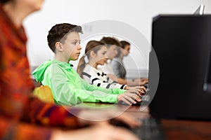 Focused tween boy studying with classmates in computer lab