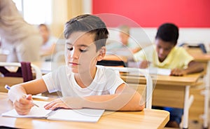 Focused tween boy writing exercises in classroom during lesson