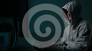 Focused unrecognizable man hacker wearing sweatshirt with hood typing on desktop computer keyboard breaking password