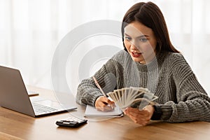 Focused woman budgeting with cash and calculator at desk