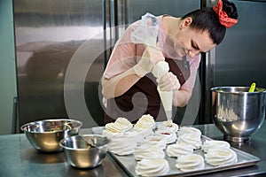 Focused woman confectioner decorating set of merengue nests with custard photo