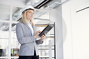 Focused woman in formal wear and hardhat using tablet at work