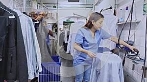 Focused woman laundry worker ironing shirt at dry-cleaning store