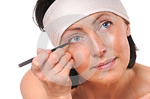 Focused woman looking at camera while putting eyeliner
