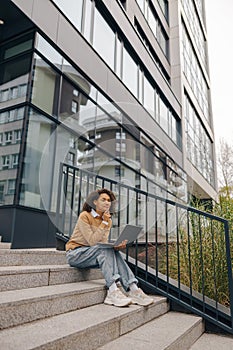 Focused woman manager working laptop sitting on stairs on modern building background