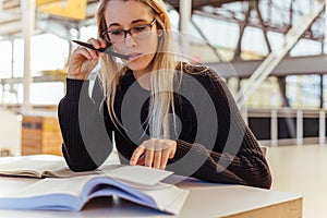 Focused woman reading books on desk in library