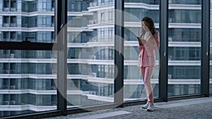 Focused woman texting phone message browsing internet in business office window.